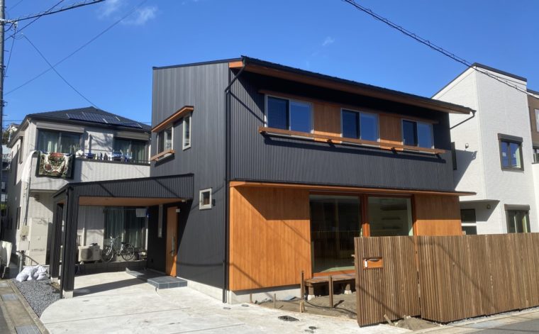 B.B.Yokosukaの家の外観。全体を黒いガルバリウム鋼板でしつらえた「Black　Base」となる精悍なフォルムに木部の鮮やかな色合いが引き立ちます。植栽も入れば緑が生えるお宅の完成です。