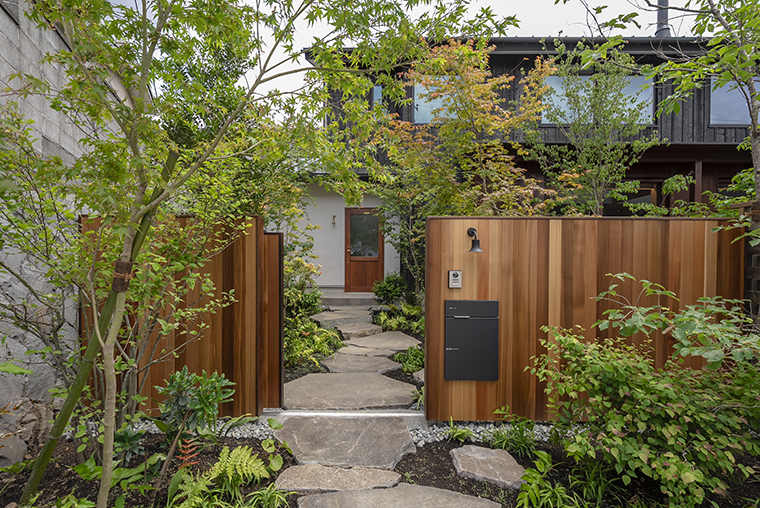 高低差を解消しつつ雑木を配した外構。大きな鉄平石のアプローチが家までの動線を楽しめます。