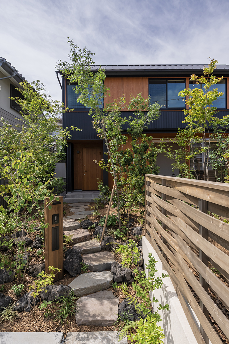 庭木のまわりは風情のある黒の溶岩石を積み、アプローチには鉄平石を使って、高低差と奥行き感を楽しめます。下草や植栽の鮮やかな緑が映え、瑞々しい潤いのある空間です。